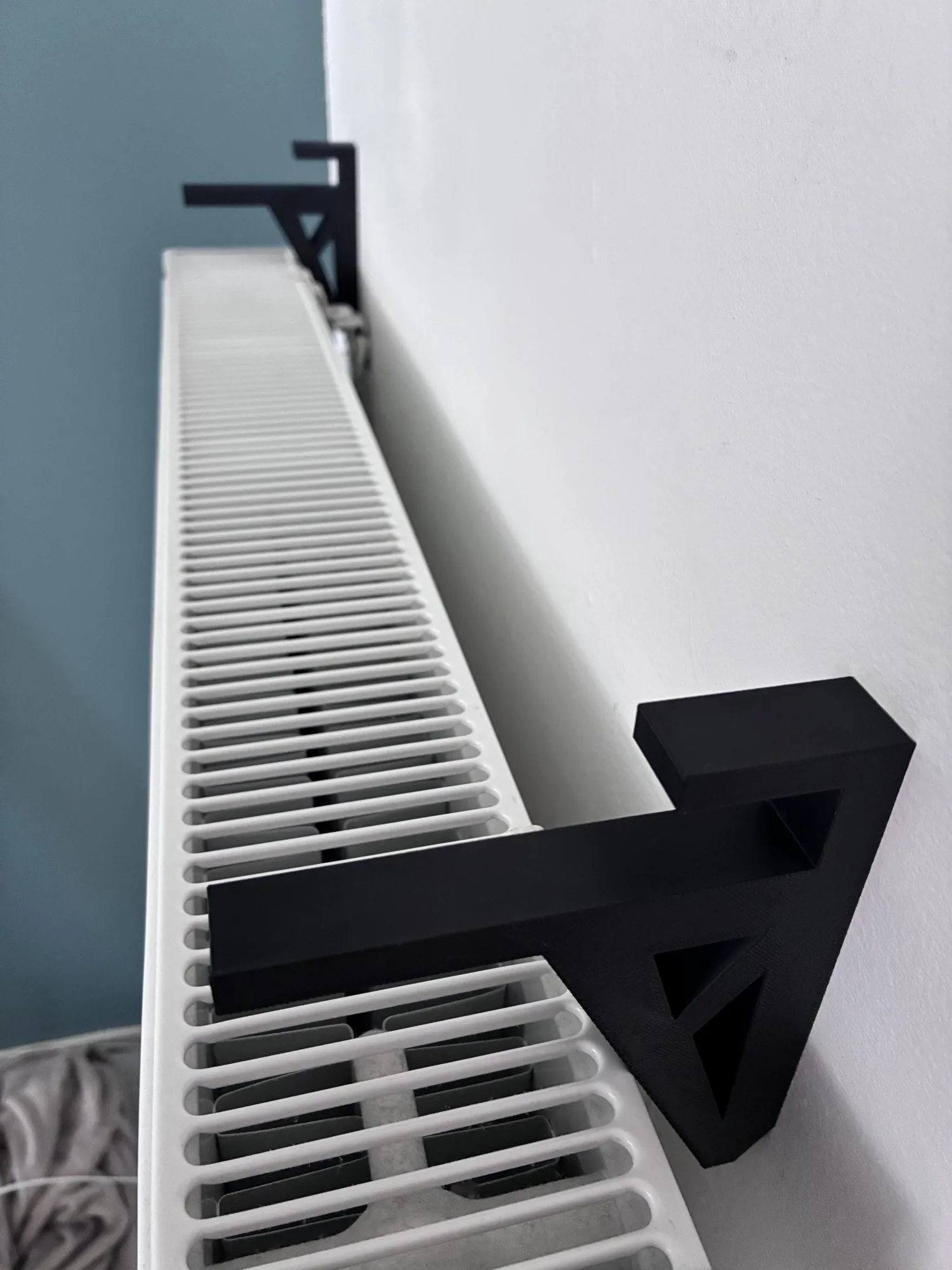 Deux équerres noires posées sur un radiateur blanc, contre un mur clair