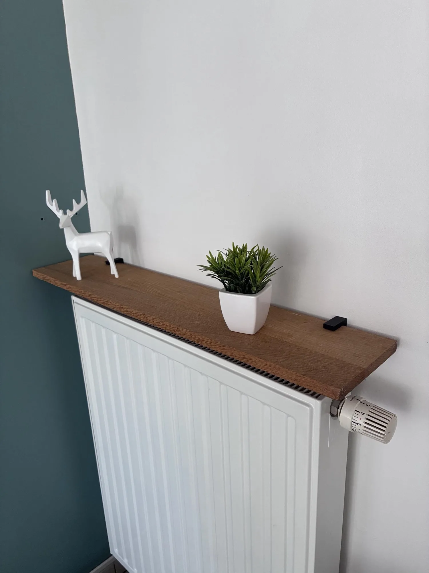 Une planche en bois posée sur deux équerres au-dessus d'un radiateur blanc
