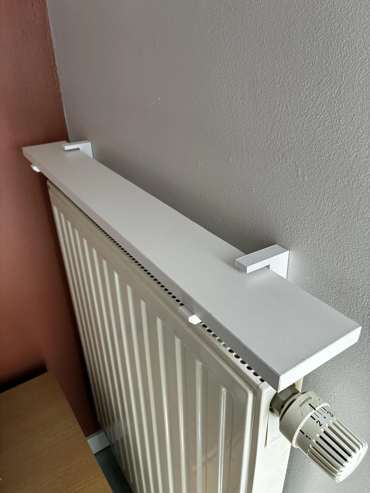 Une étagère blanche posée sur un radiateur à ailettes verticales