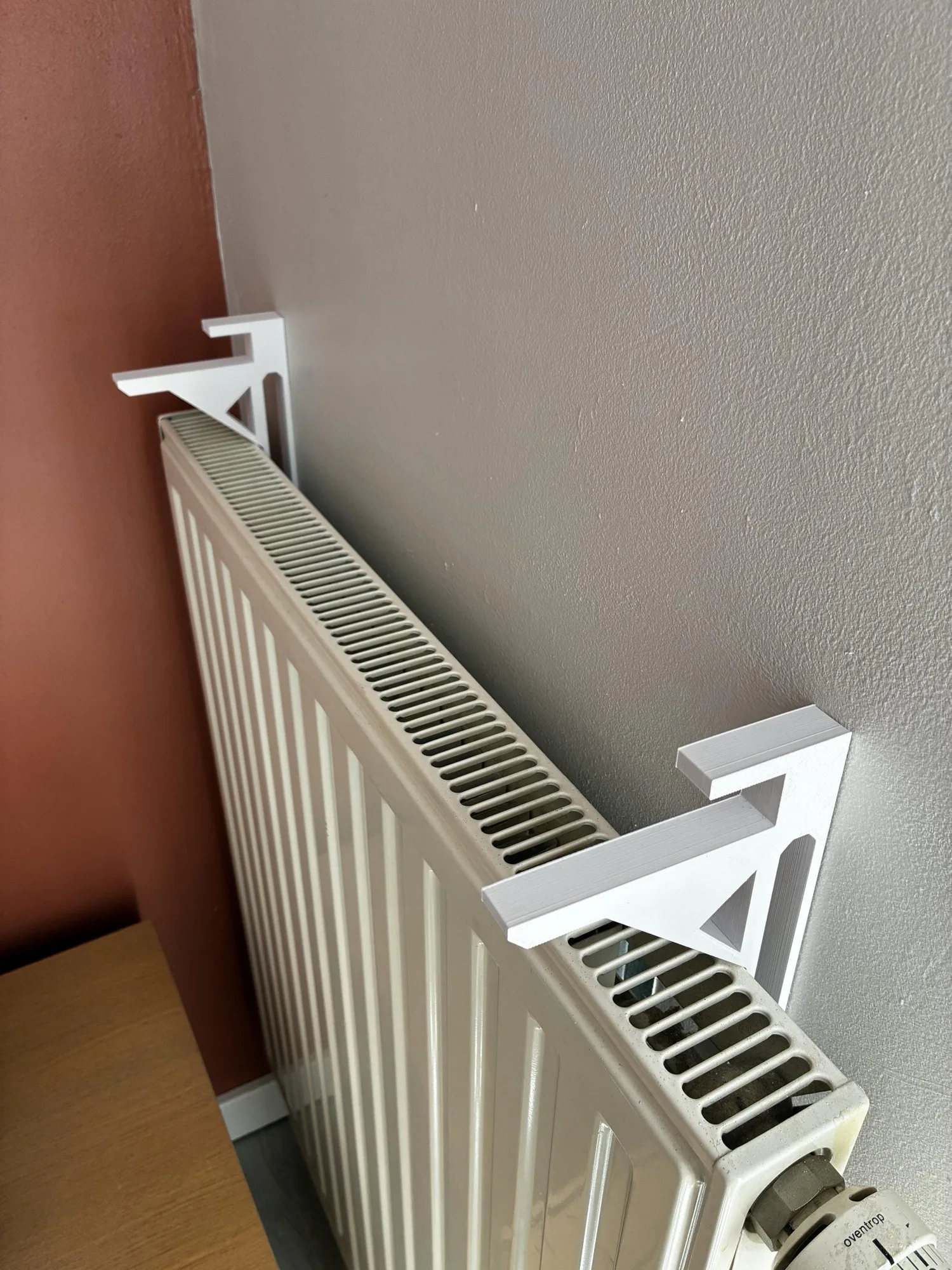 Deux équerres blanches en place sur le dessus d'un radiateur crème